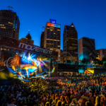 `Movement Detroit 2026 at Hart Plaza, with thousands of fans gathered under a vibrant light show against the illuminated Detroit skyline during the festival's 20th anniversary edition.`