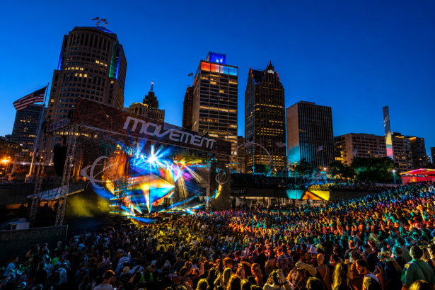 `Movement Detroit 2026 at Hart Plaza, with thousands of fans gathered under a vibrant light show against the illuminated Detroit skyline during the festival's 20th anniversary edition.`