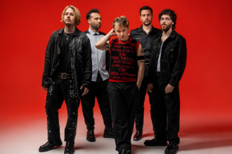Nothing But Thieves pose against a bold red background in a 2026 press photo, ahead of their fifth studio album 'Stray Dogs' and biggest ever headline world tour.