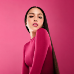 `Olivia Rodrigo poses in a pink long-sleeve top against a pink background, promoting her 2026 album 'You Seem Pretty Sad for a Girl So in Love.'`