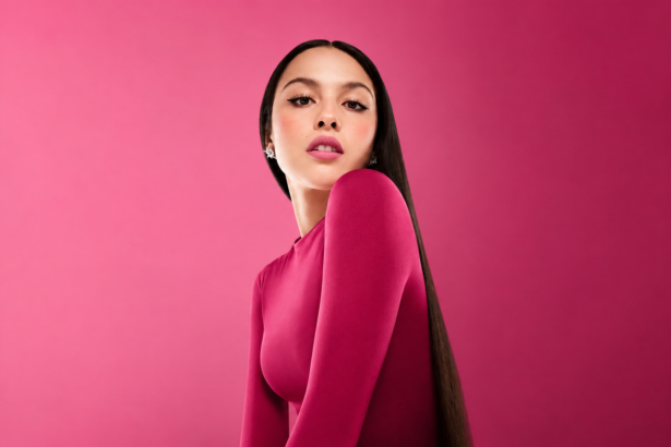 `Olivia Rodrigo poses in a pink long-sleeve top against a pink background, promoting her 2026 album 'You Seem Pretty Sad for a Girl So in Love.'`