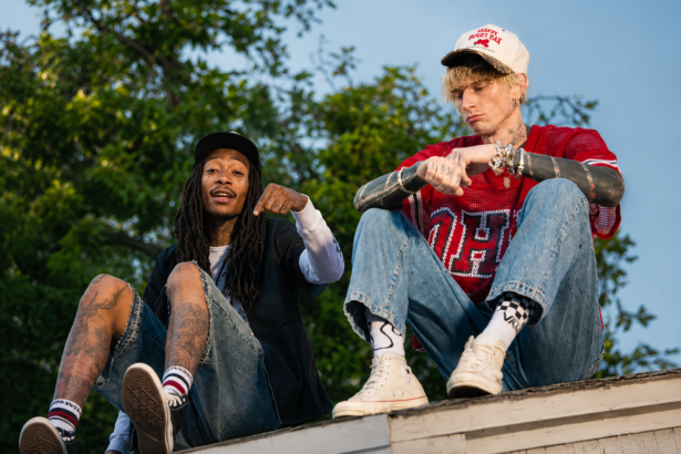 `Wiz Khalifa and mgk sitting on a rooftop in a still from the 'Girl Next Door' music video, with trees and an open sky behind them.`
