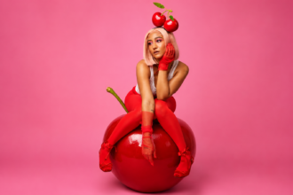 Camryn Levert in a cherry-themed red editorial look seated on a giant cherry prop with a cherry crown headpiece for the official cover art of her 2026 single cherry
