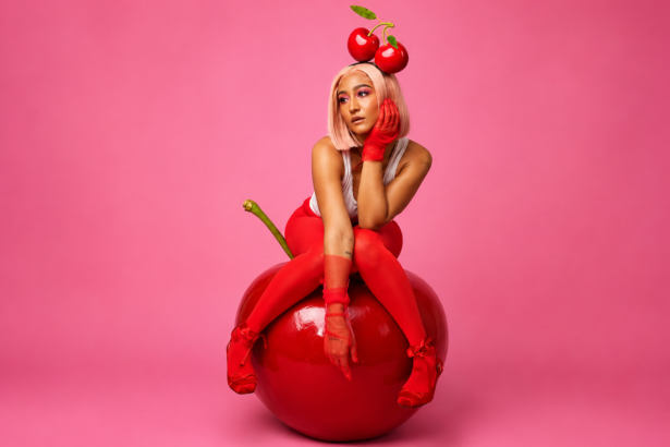 Camryn Levert in a cherry-themed red editorial look seated on a giant cherry prop with a cherry crown headpiece for the official cover art of her 2026 single cherry