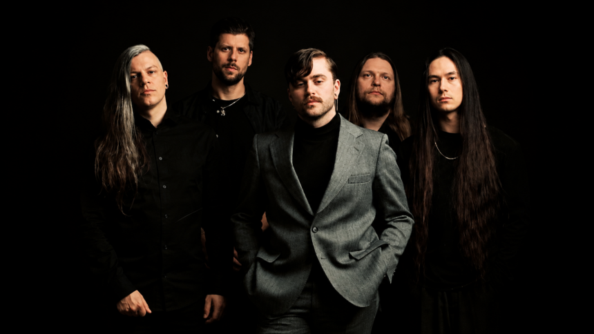 Imminence band press photo 2026 — five members posed against a dark background, with frontman Eddie Berg centered in a grey suit and black turtleneck, flanked by bandmates dressed in black