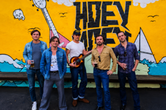 Jet band posing in front of a colorful mural in Melbourne, Australia, with five members standing casually outdoors
