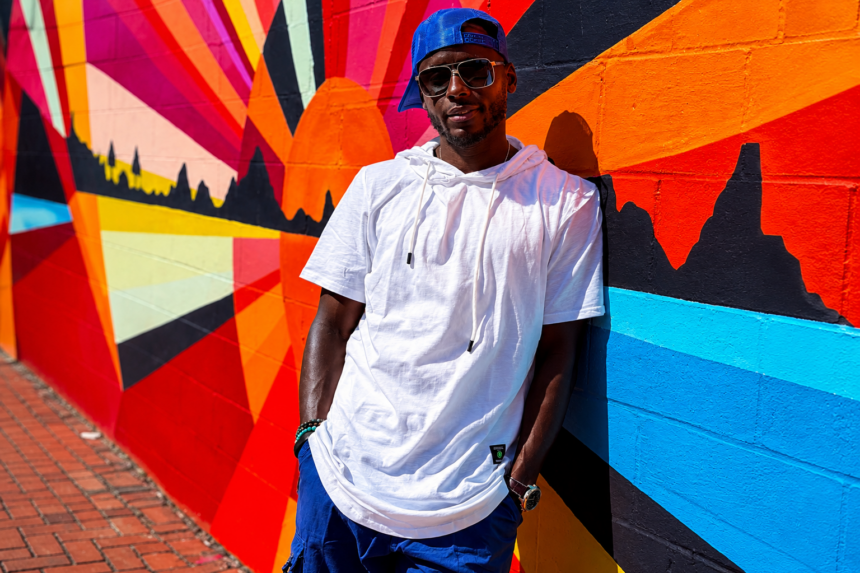 Kentucky hip-hop artist Josh Garnett in a white hoodie and blue snapback leaning against a colorful street mural around the May 2026 release of his single Show You How