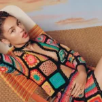 Olivia Rodrigo poses in a vibrant crocheted ensemble on a retro-style lounge chair.