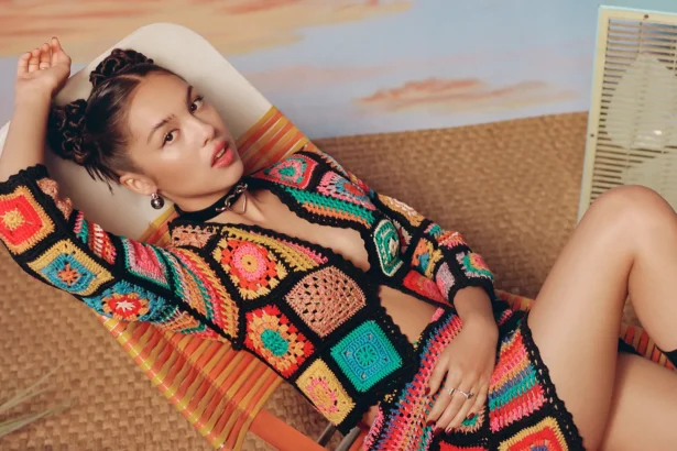 Olivia Rodrigo poses in a vibrant crocheted ensemble on a retro-style lounge chair.