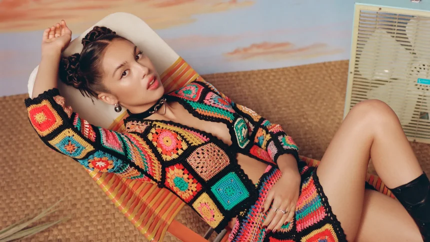 Olivia Rodrigo poses in a vibrant crocheted ensemble on a retro-style lounge chair.