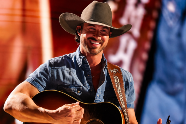 Riley Green performing live in 2026 wearing his Duck Club guitar strap, the same tour cycle as his Toby Keith tribute single Think As You Drunk