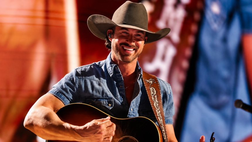 Riley Green performing live in 2026 wearing his Duck Club guitar strap, the same tour cycle as his Toby Keith tribute single Think As You Drunk