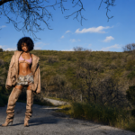 Tyla in a high-fashion outdoor editorial shoot, standing on a countryside road beneath a blue sky.
