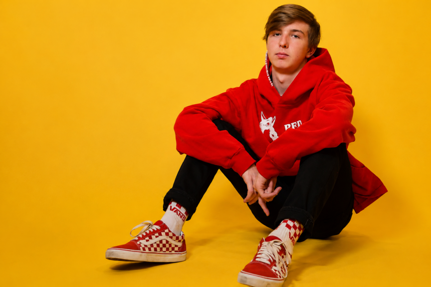 Electronic music producer Whethan in a red hoodie and checkered Vans sneakers posed against a yellow studio background ahead of his 2026 WAREHOUSE.WAVS Tour across North America