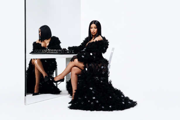 A woman wearing an elegant black feathered gown sits confidently beside a white table with a chess set in a minimalist white studio.