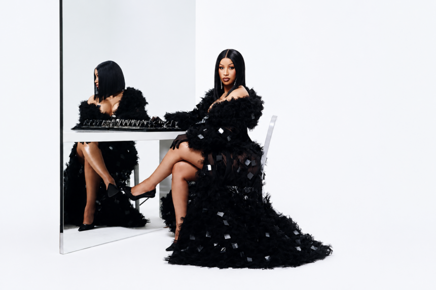 A woman wearing an elegant black feathered gown sits confidently beside a white table with a chess set in a minimalist white studio.