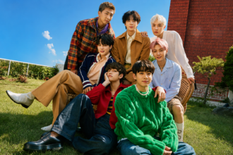 BTS members posing together outdoors in a colorful group portrait on a sunny day.