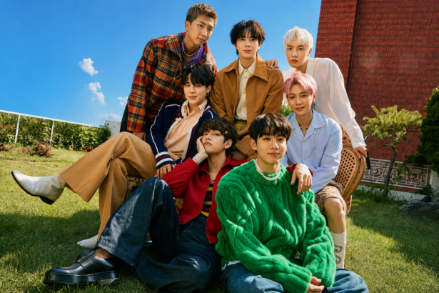 BTS members posing together outdoors in a colorful group portrait on a sunny day.