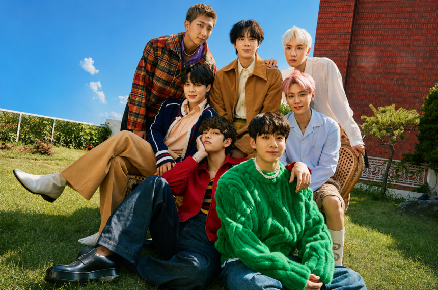 BTS members posing together outdoors in a colorful group portrait on a sunny day.