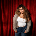 Bella Kay, whose single 'i deserve better.' closes her debut album 'My Reckless Abandon,' photographed against a red curtain.
