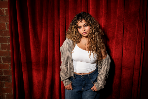 Bella Kay, whose single 'i deserve better.' closes her debut album 'My Reckless Abandon,' photographed against a red curtain.