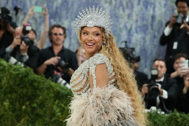 Beyoncé smiling over her shoulder at the Met Gala in a crystal headpiece and feathered gown, with photographers behind her