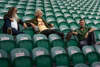 Cast's trio lounging in empty stadium seats in a press photo ahead of their 2026 'Yeah Yeah Yeah' UK tour