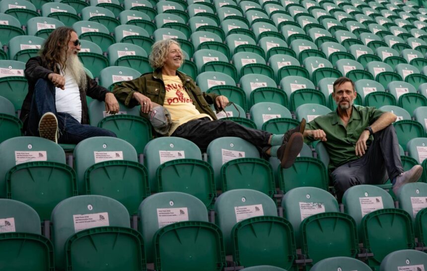 Cast's trio lounging in empty stadium seats in a press photo ahead of their 2026 'Yeah Yeah Yeah' UK tour