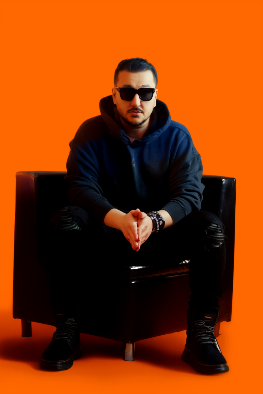 Daijo wearing a dark hoodie and sunglasses while seated in a black armchair against a vibrant orange background