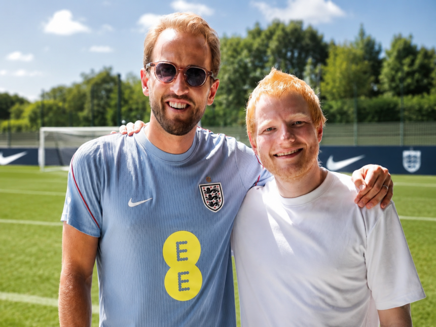 Ed Sheeran and Harry Kane smiling with arms around each other on an England training pitch