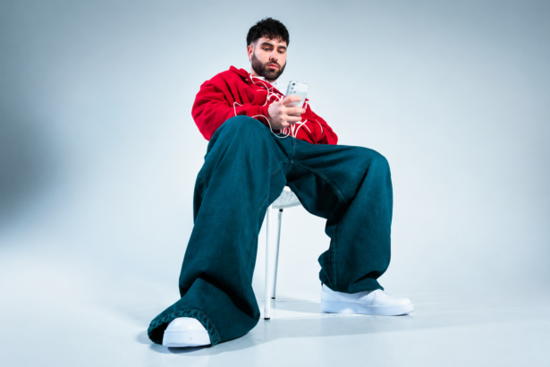 Fat Papi sitting on a white chair in a minimalist studio, wearing a red hoodie