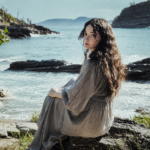 Gloria de Oliveira sitting by the seaside on a rocky shore.