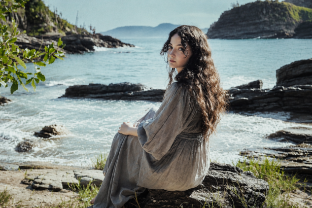 Gloria de Oliveira sitting by the seaside on a rocky shore.