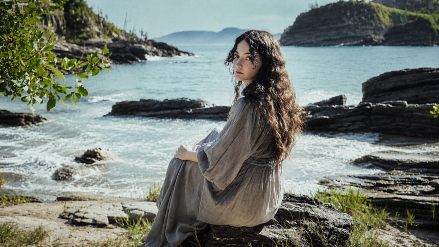Gloria de Oliveira sitting by the seaside on a rocky shore.