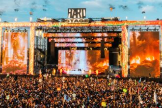 Massive crowd gathered at the HARD Stage during HARD Summer Music Festival, with pyrotechnics and giant LED screens lighting up the main stage at sunset