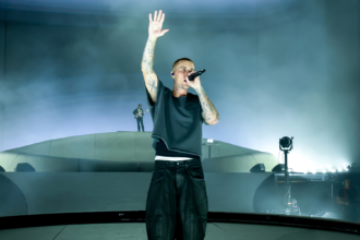 Justin Bieber, newly confirmed for the 2026 World Cup final halftime show, performs live on stage with his hand raised while singing into a microphone.