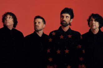 The four members of Kasabian pose in black outfits against a red backdrop in a press photo announcing the 'Nothing Better Than This' UK arena tour.
