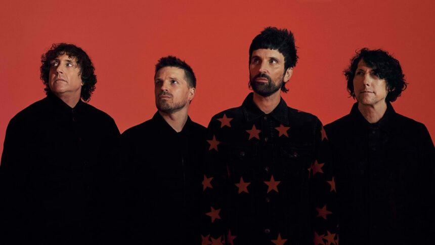 The four members of Kasabian pose in black outfits against a red backdrop in a press photo announcing the 'Nothing Better Than This' UK arena tour.