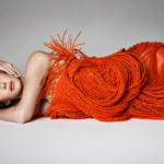 Lana Del Rey reclines in a sculptural orange fringe gown ahead of her new albums Stove and its companion record Spyda.