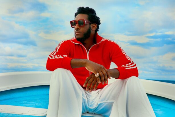 Leon Bridges sits on the deck of a boat wearing a red track jacket and sunglasses, announcing his new album Happiness Anytime