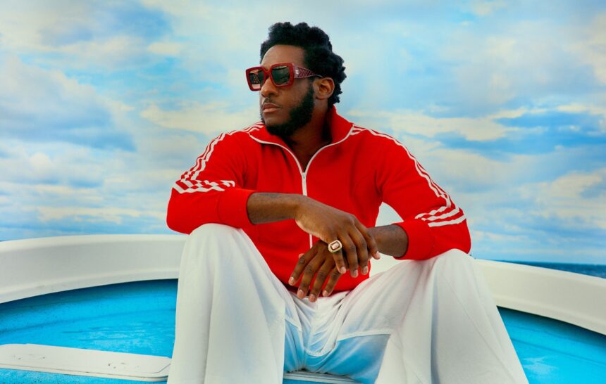 Leon Bridges sits on the deck of a boat wearing a red track jacket and sunglasses, announcing his new album Happiness Anytime