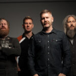 Mastodon band members pose for a studio portrait against a gray backdrop.