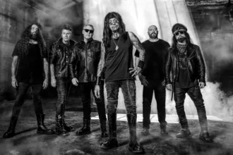 Ministry photographed in black and white in an industrial space, frontman Al Jourgensen at center in a warehouse haze