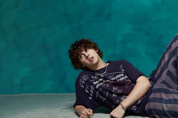 NOAHFINNCE Noah Adams lying on a studio floor wearing a graphic-print t-shirt and layered jewelry, promotional image for his Mr Overwhelm UK Tour in October 2026