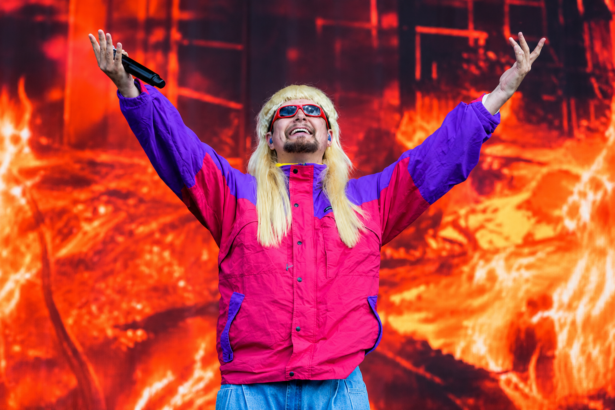 Oliver Tree performs onstage with arms raised, wearing a blond mullet wig and pink and purple windbreaker
