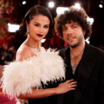Selena Gomez and Benny Blanco pose together on a red carpet, Gomez in a white feathered dress