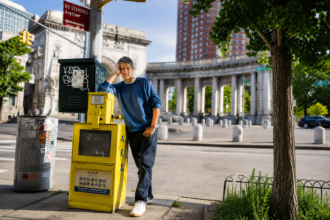 Mike D leans against a yellow newspaper box on a New York City street in a blue sweatshirt and jeans, in press art for his solo debut album 'Thank You.'