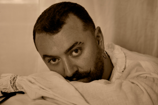 Sam Smith rests their head on soft fabric in a warm-toned close-up portrait, in press art for their fifth album 'Hazel Eyes.'
