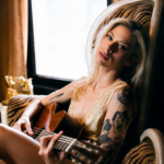 Andie Case, whose single 'Better Days' previews her debut EP, holds an acoustic guitar in a warmly lit portrait.