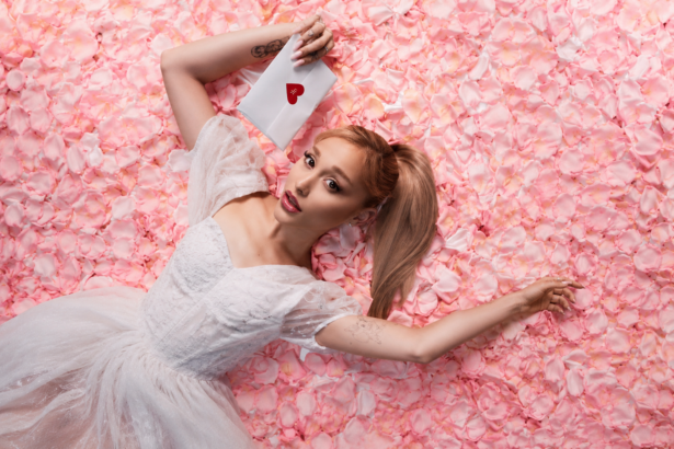 Ariana Grande, whose album 'petal' debuted at No. 1, lies on pink rose petals in a white dress holding a heart-sealed envelope.